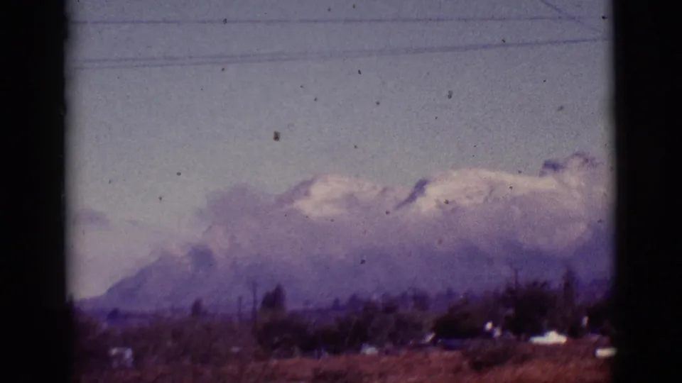 1965 8mm view near Tuscon, Arizona, showing hazy snow-capped mountains behind rural grassland and overhead utility lines.
