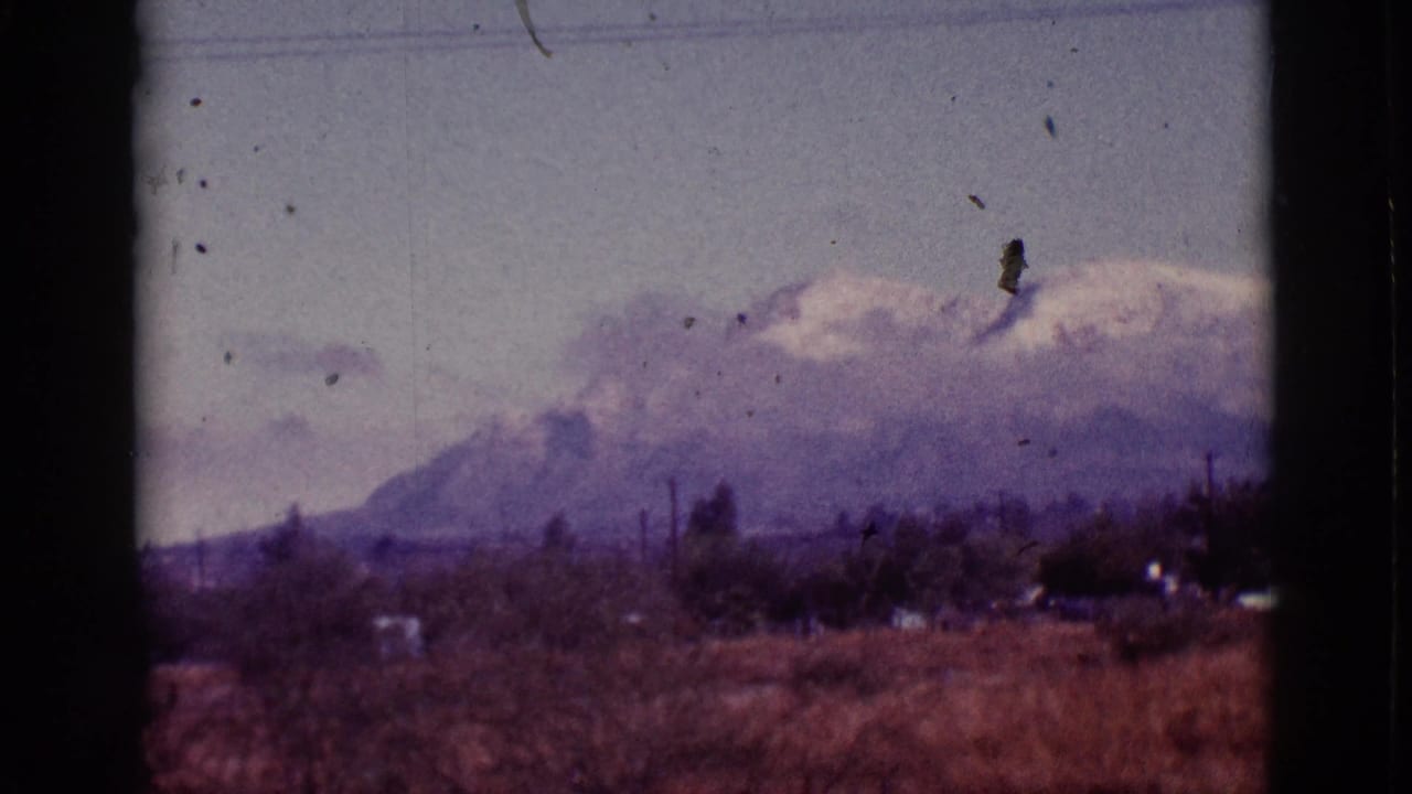 Hazy mountain range with snow patches, dry foreground brush, utility lines, and dark film gate edges.