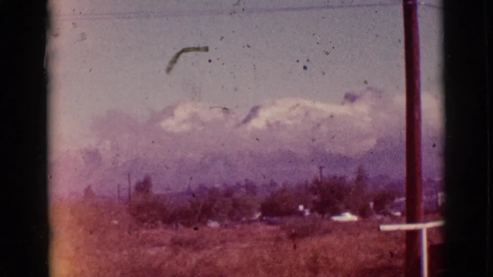 1965 8mm Tuscon-area landscape with snow-capped mountains, a purple color cast, dry rural foreground, and a utility pole at the edge.