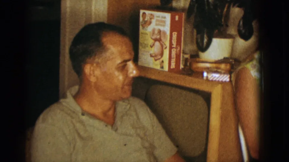 1966 Clarkdale home-movie frame showing a man in a light polo shirt near a TV console with a visible cereal box.