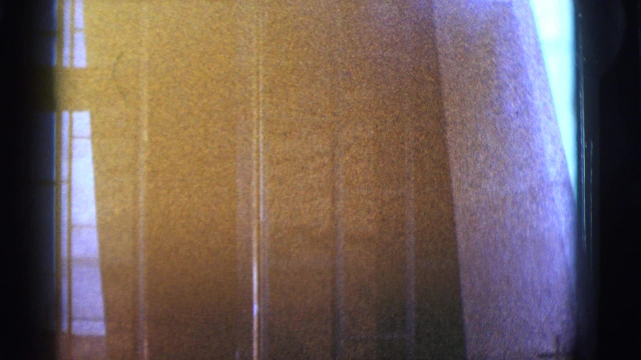 Close view of a textured building surface with narrow vertical glass and heavy film shadowing.