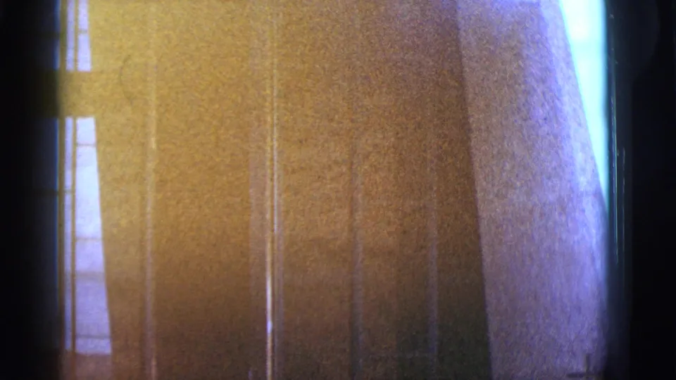 1966 Clarkdale, Arizona home-movie frame showing a close exterior building detail with glass, wall texture, light leak, and dark film edges.