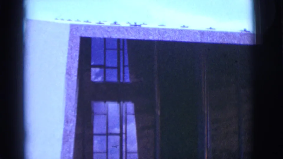 1966 Clarkdale, Arizona home-movie frame showing a cropped facade with tall window panes, dark framing, and strong blue color shift.