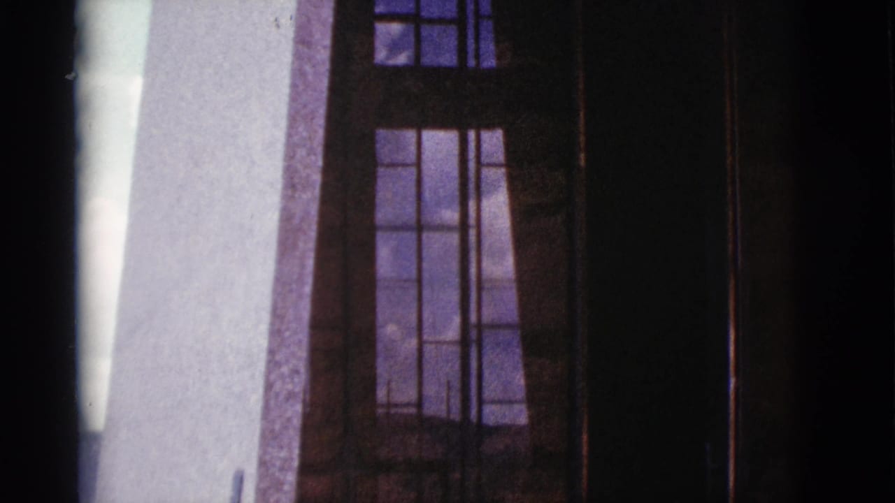 Tall gridded windows in a stone building facade with dark vertical edges.