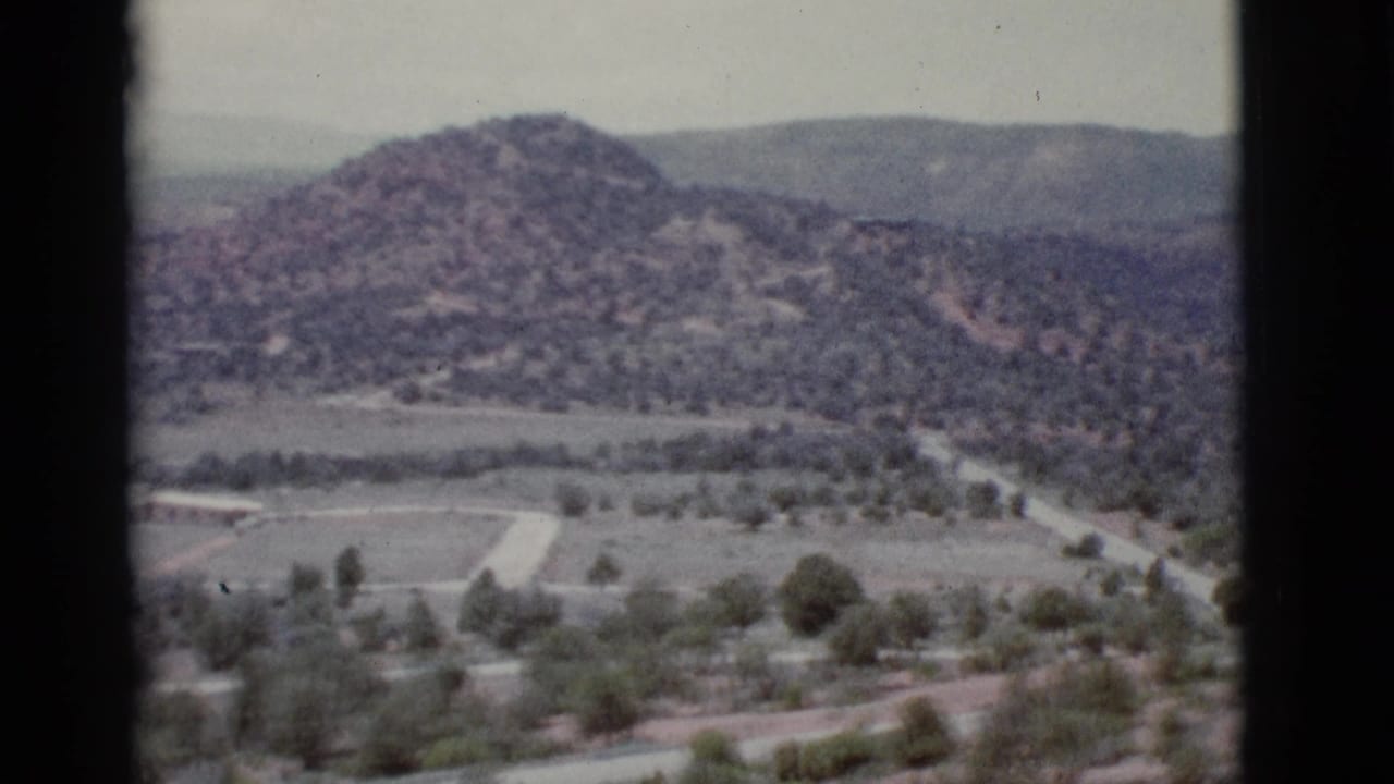 Wide hazy view of desert hills, valley trees, pale roads, and distant mountains.