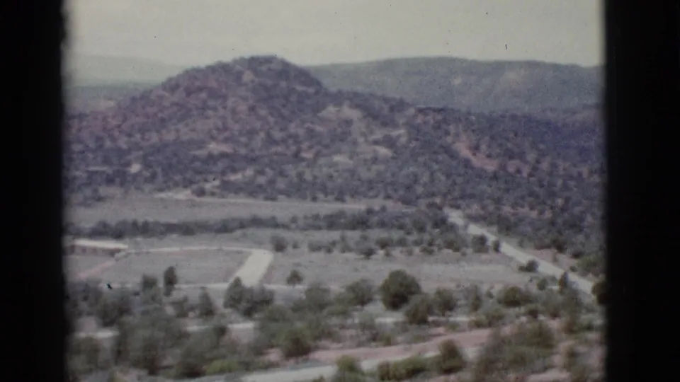 1966 8mm view near Clarkdale, Arizona, showing a hazy valley with scattered trees, low hills, pale roads, and distant mountain ridges.