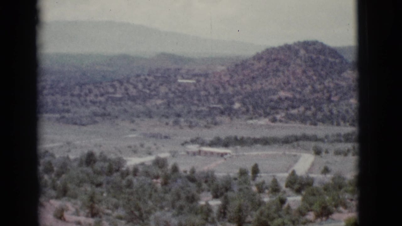 Clarkdale, Arizona home-movie frame with a rounded desert hill, scattered green trees, pale road lines, and soft mountains in the distance.