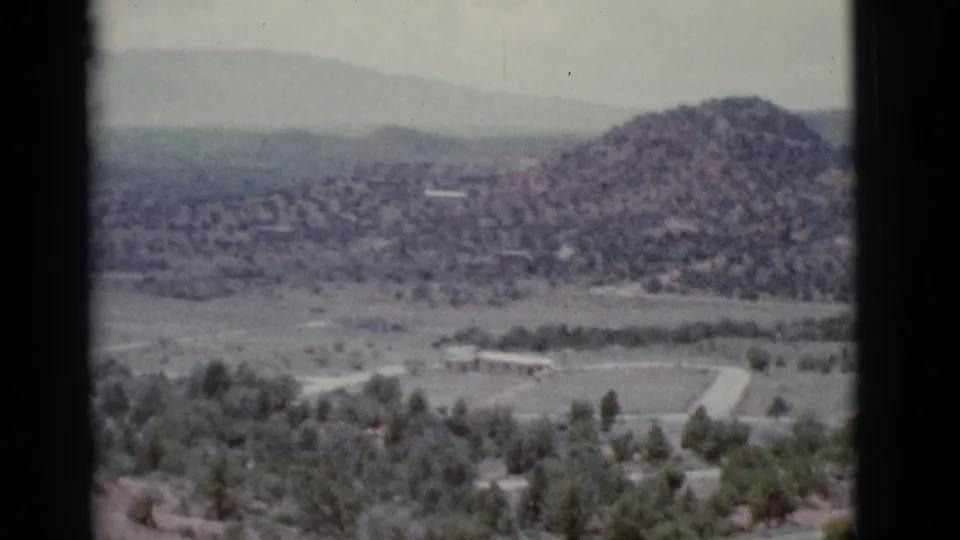 Clarkdale, Arizona home-movie frame with a rounded desert hill, scattered green trees, pale road lines, and soft mountains in the distance.