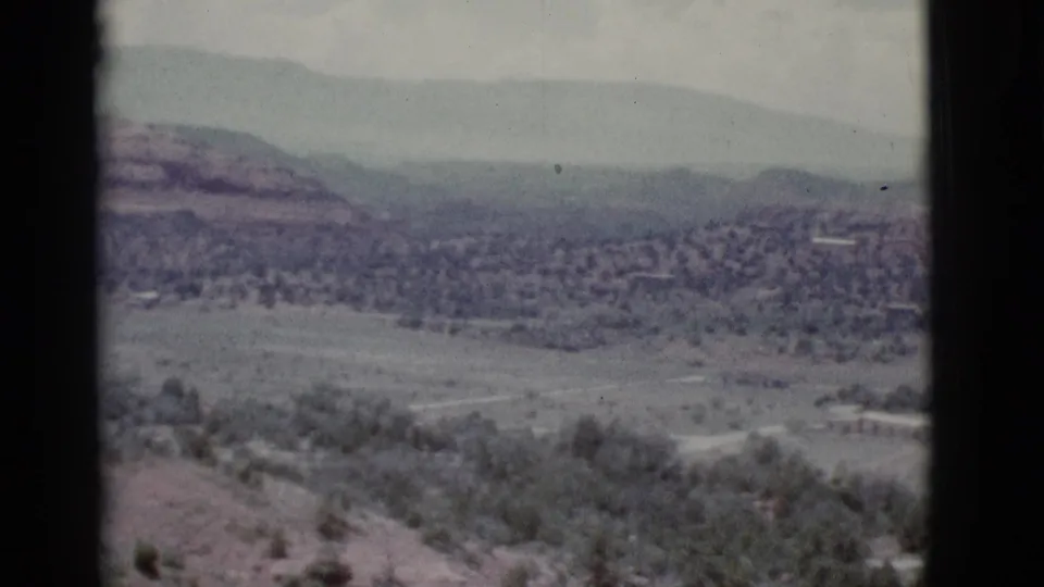 Faded 8mm frame from the Clarkdale-area panorama, showing open desert valley, scattered trees, low hills, and layered mountain ridges.