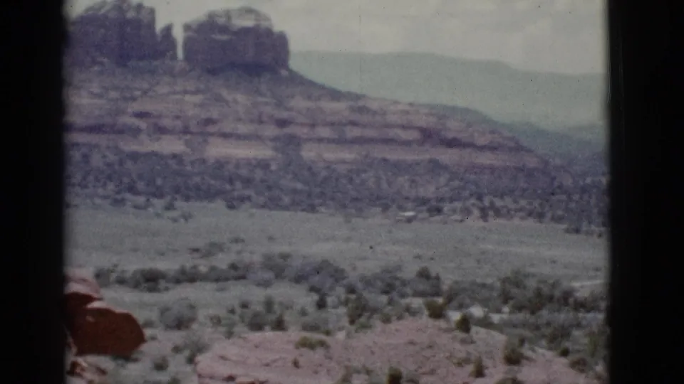 1966 Clarkdale-area frame showing a red rock formation rising above a tree-dotted desert valley and distant hazy mountain ridges.