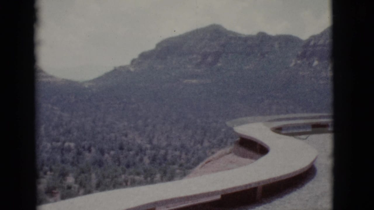 Curved overlook edge in front of scrub desert and distant rocky hills.
