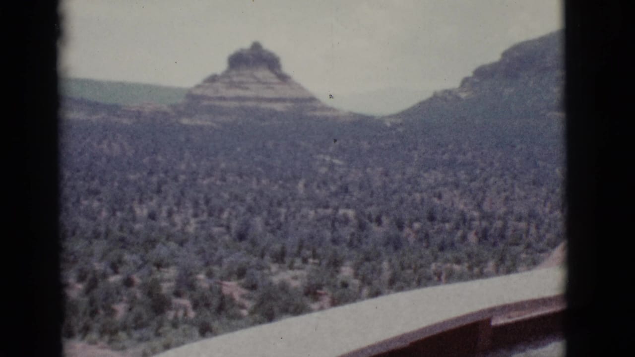 Pointed layered butte rising beyond a broad field of desert shrubs.