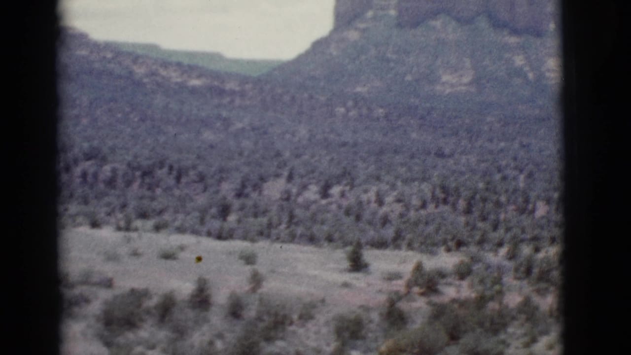 Soft 8mm view of a scrub valley below layered mountains and pale sky.