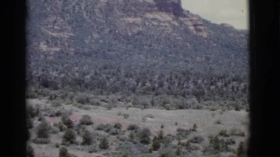 1966 Clarkdale, Arizona 8mm frame showing scrub trees and open ground below a rocky mountain slope.