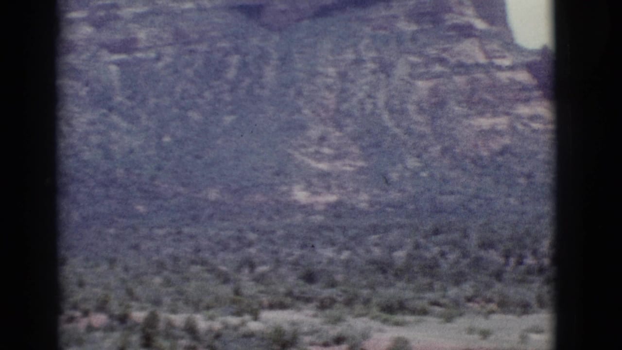 Red rock canyon walls and desert vegetation seen through dark 8mm film-frame edges.