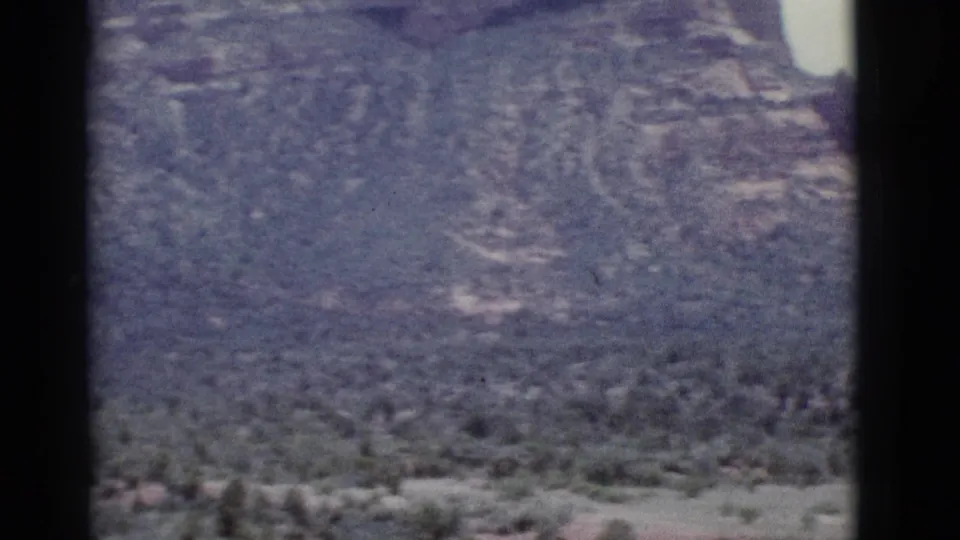 1966 8mm view near Clarkdale, Arizona, showing layered canyon cliffs, scrub vegetation, pale sky, and visible film gate borders.
