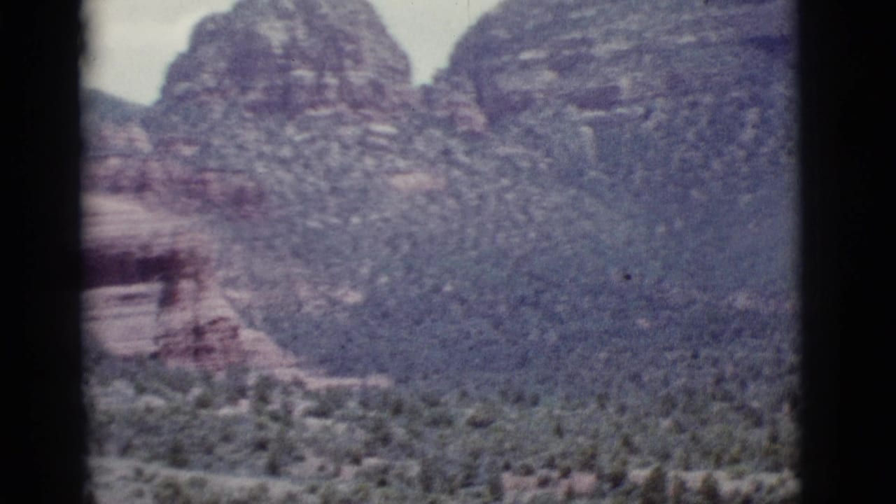 Distant sandstone cliffs and desert brush partially divided by a dark vertical film edge.
