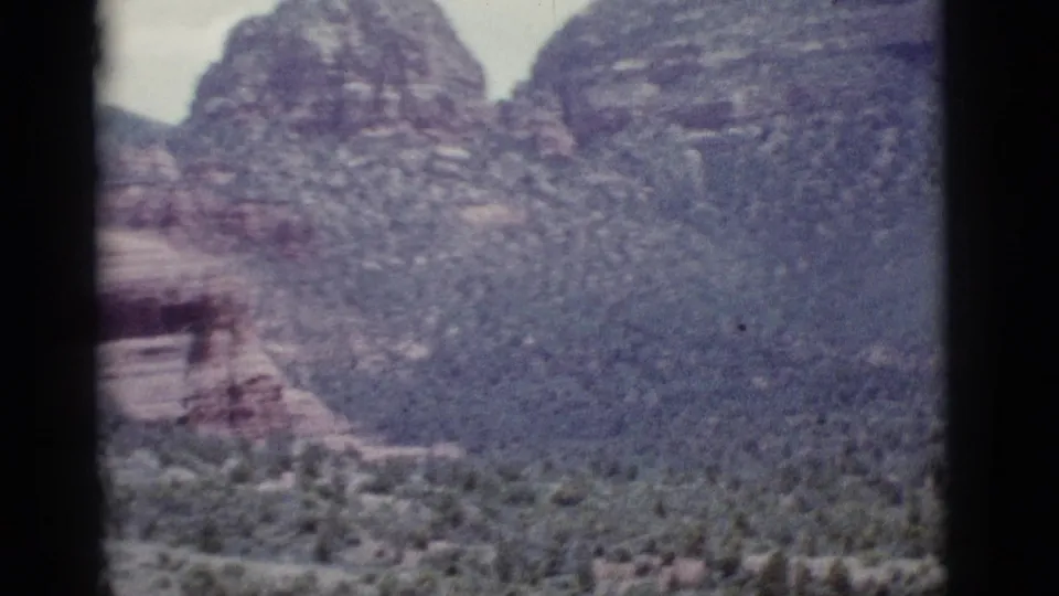 Mid-pan 1966 8mm frame near Clarkdale with distant red rock formations, scrubland, pale sky, and a dark vertical gate line.