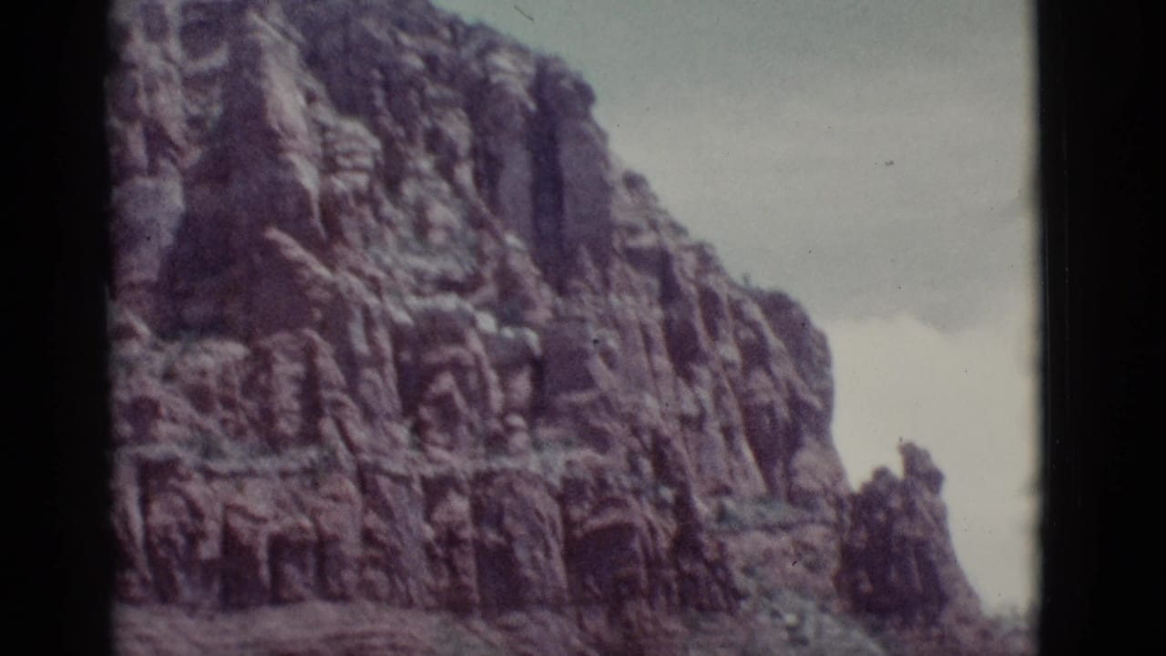 1966 Clarkdale, Arizona 8mm frame with a tall layered red rock wall and sparse vegetation at its base.