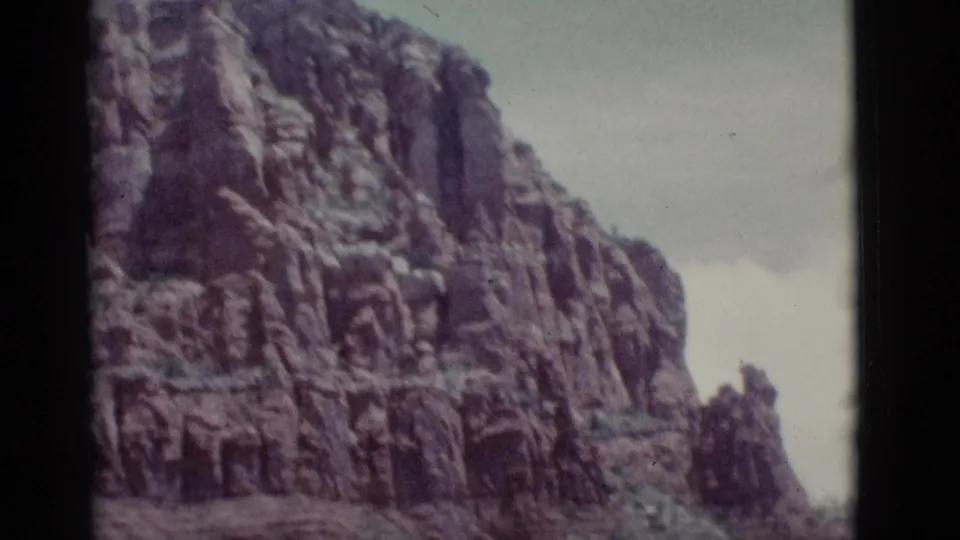 1966 Clarkdale, Arizona 8mm frame with a tall layered red rock wall and sparse vegetation at its base.