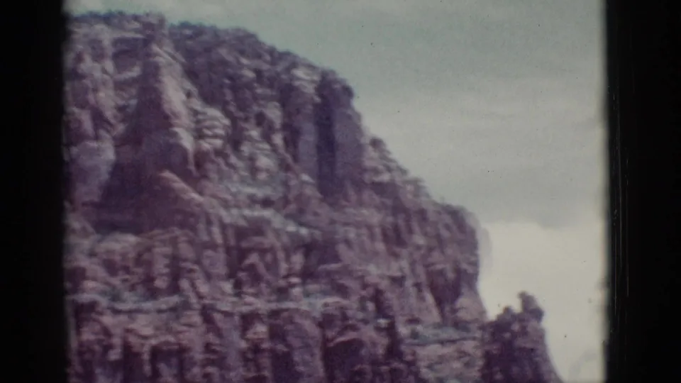 1966 Clarkdale, Arizona 8mm frame showing a broad red rock cliff face and smaller outcrops beneath a hazy sky.