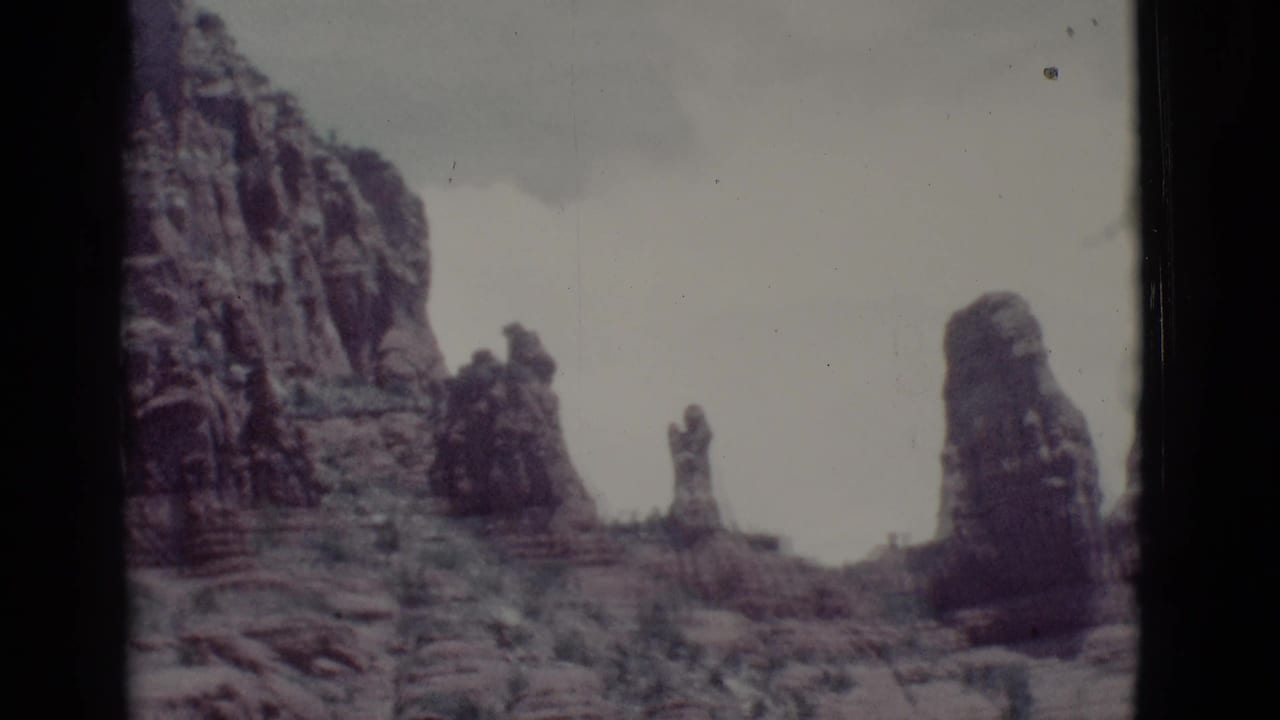 Tall desert rock formations under a pale sky with dark film borders.