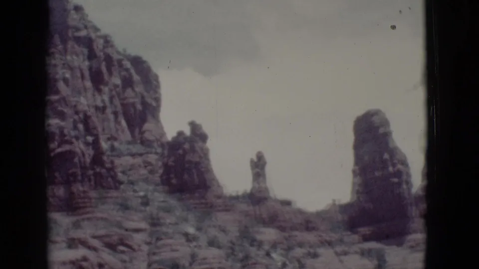 1966 Clarkdale-area home-movie frame showing rugged desert rock spires and cliff faces under a muted sky.