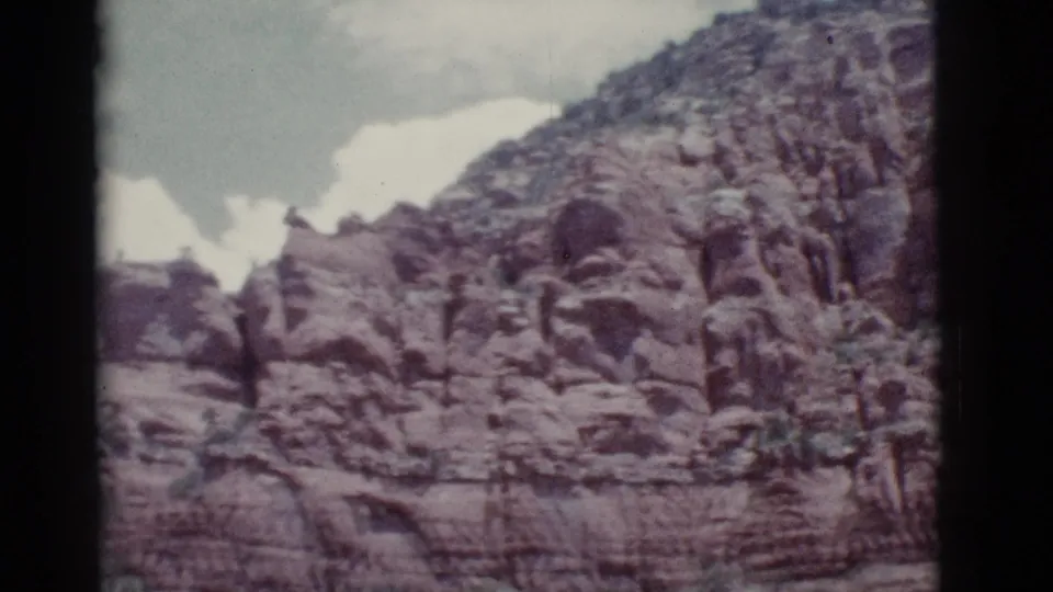 Vintage 8mm view of a rocky Arizona hillside, with weathered formations below a bright clouded sky.