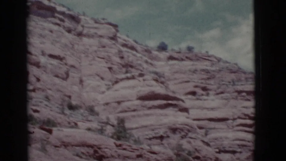 A handheld 1966 8mm frame shows a sloping Clarkdale rocky hillside with rounded ledges, sparse shrubs, and muted sky.