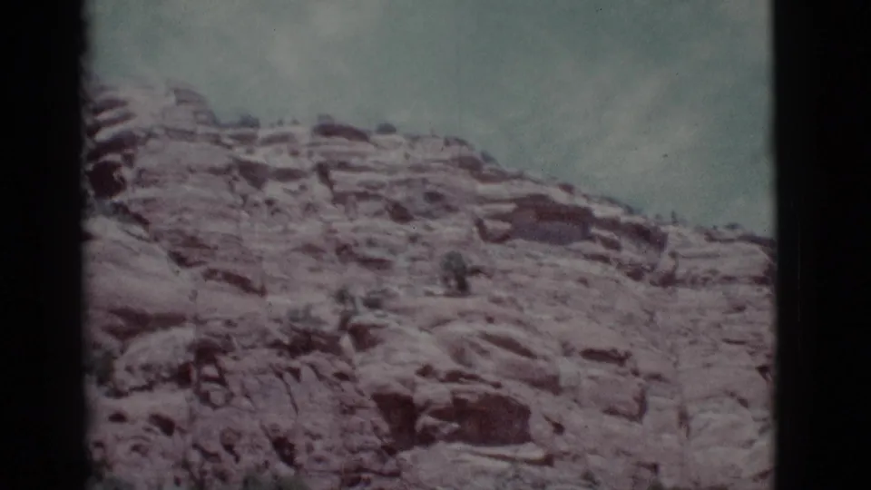 Faded 8mm view of a broad Arizona rock slope near Clarkdale, with layered stone, scattered shrubs, and pale cloudy sky.