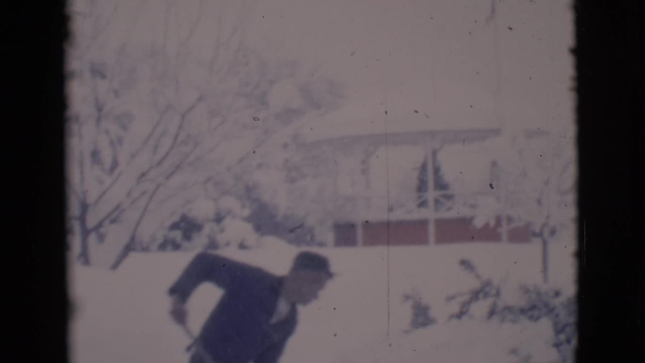 In 1966 Clarkdale, Arizona, a man in a dark coat and hat appears to shovel deep snow in a residential yard.