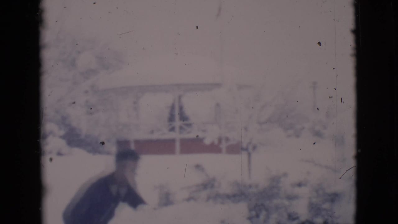 Man shovels snow as the camera begins to pan right across the snowy yard.