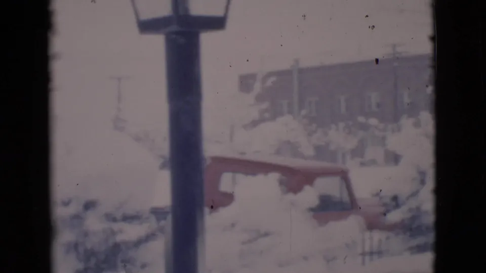 The pan settles on a lamppost, a partially snow-covered red vehicle, and a house in Clarkdale, Arizona, 1966.