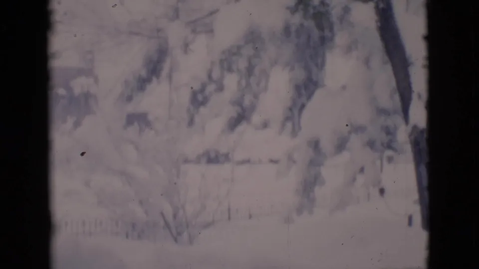 Clarkdale winter home-movie frame with snow-laden yard details, bare trees, fence lines, and a dark foreground edge.