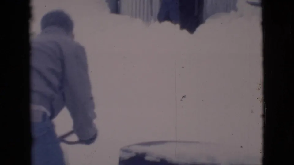 1966 8mm frame from Clarkdale, Arizona, showing a man bending with a shovel in a snowy yard.