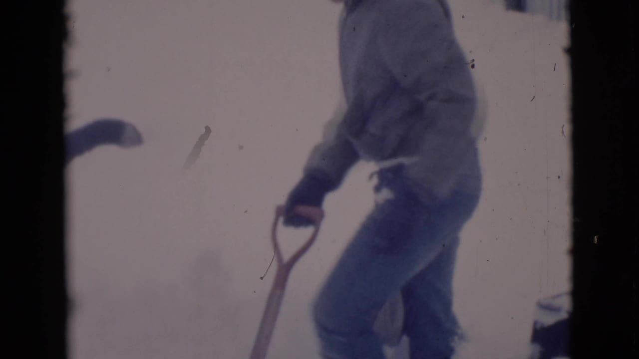 Man in heavy clothing holds a shovel near a snowy surface.