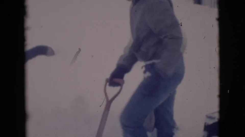 1966 8mm frame from Clarkdale, Arizona, with a bundled man using a shovel in a snow-covered yard.