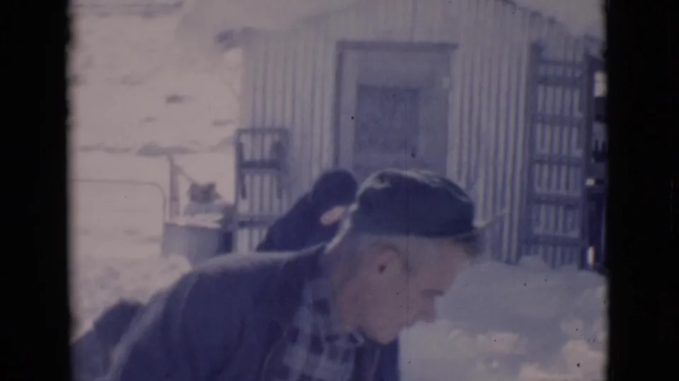 1966 8mm frame from Clarkdale, Arizona, showing a man in a cap near snow and a corrugated outbuilding.