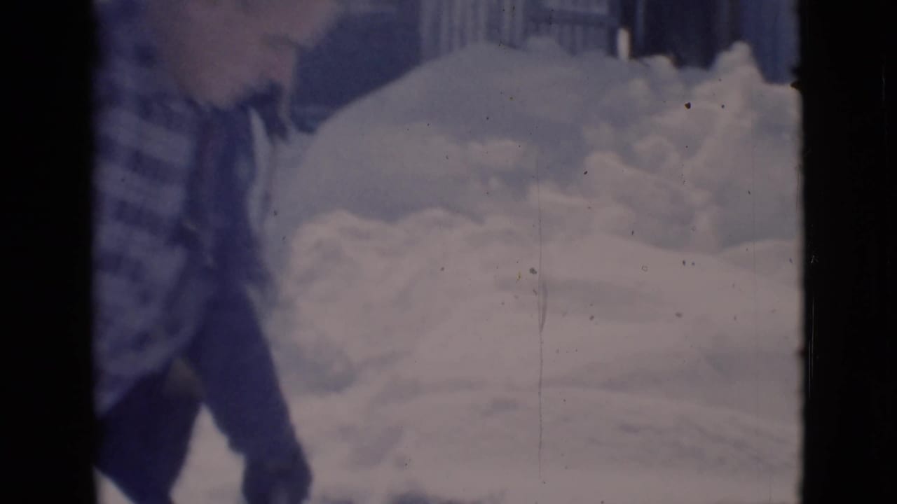 Man partly visible beside deep snow and evergreen branches in a residential yard.