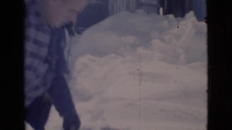 In the 1966 Clarkdale home-movie footage, a man is partly framed near deep snow and evergreen branches in a snowy yard.