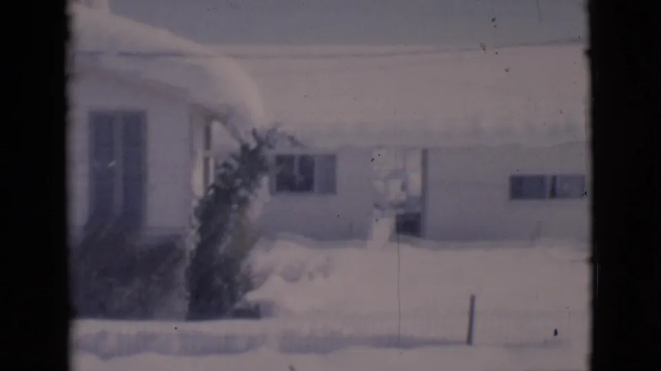 A snowy residential house exterior in Clarkdale appears as evergreen branches pass through the foreground of the 1966 8mm footage.