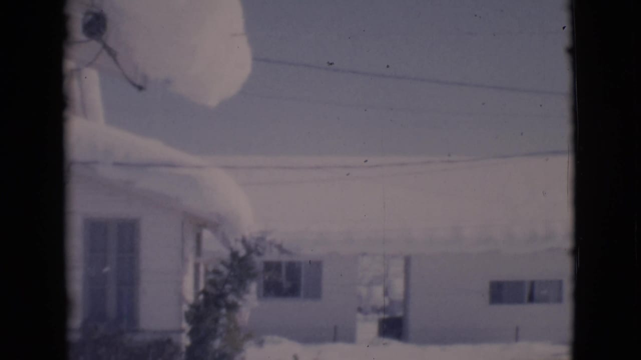 Snow-covered houses seen through dark window or film-frame edges.