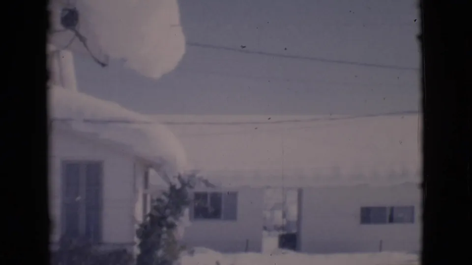 1966 Clarkdale, Arizona home-movie frame of low houses and deep snow viewed through dark vertical framing.