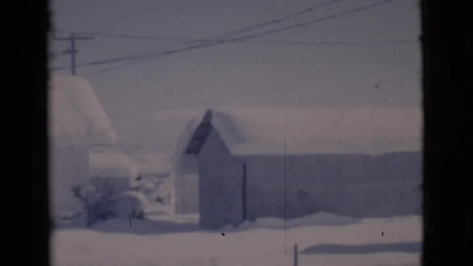 Snow-covered residential yard in Clarkdale, Arizona, with a small shed, long low building, bare shrubs, and utility wires.