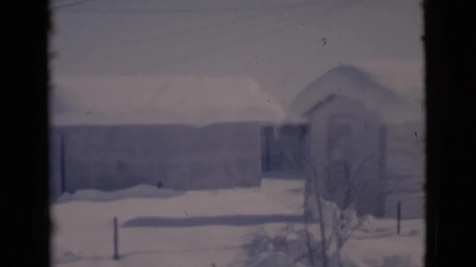Clarkdale, Arizona winter home-movie frame with a snow-covered roofline, bare tree branches, fencing, and pale overcast light.