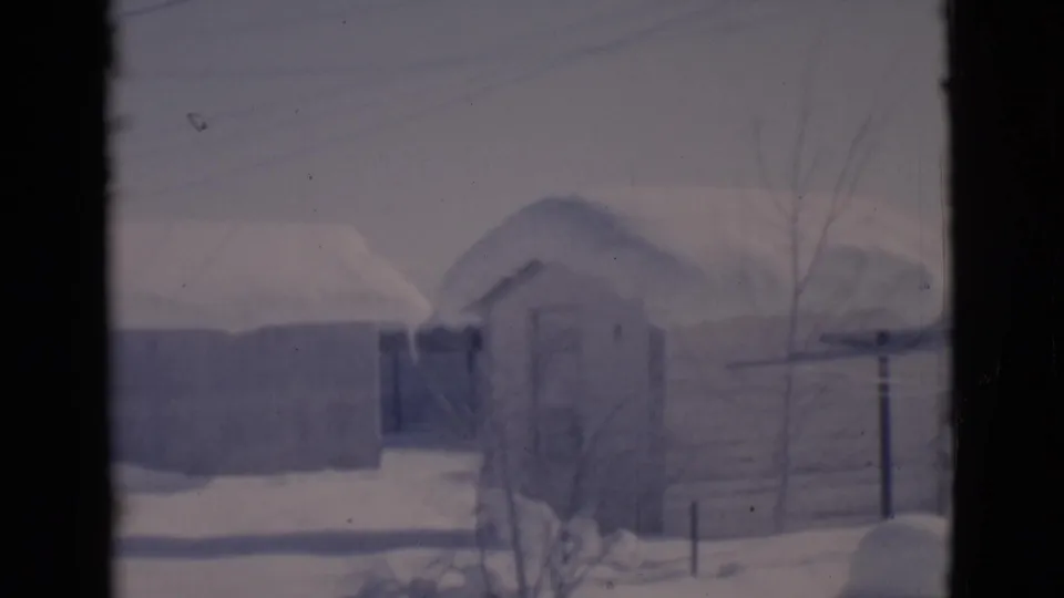 1966 Clarkdale, Arizona home-movie frame showing snowy sheds, a small outbuilding, bare branches, and dark window-like borders.