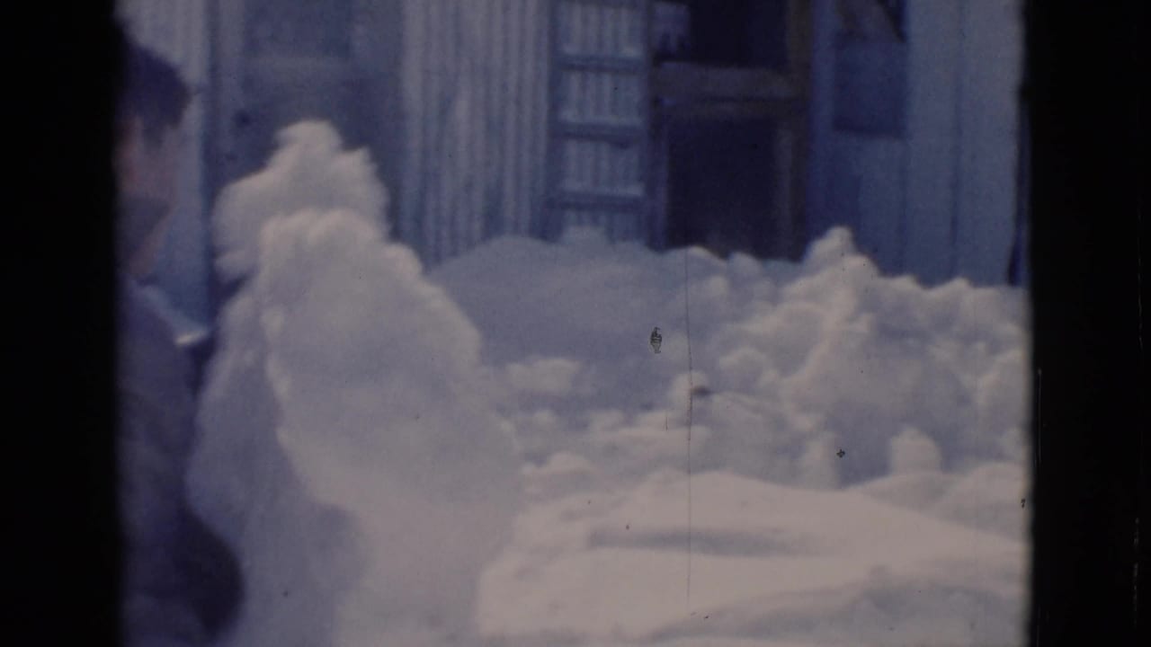 Deep snow piled beside a corrugated building with a partially visible person at the left edge.