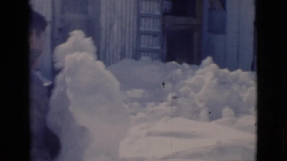 1966 Clarkdale, Arizona 8mm frame showing deep snowbanks against a corrugated structure and a partially visible person near the edge.