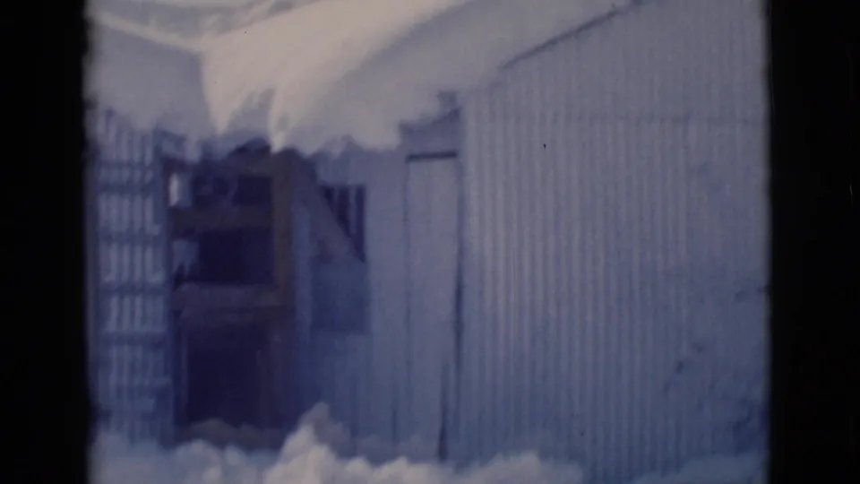 1966 Clarkdale, Arizona 8mm frame showing snow packed around a corrugated building wall and a dark doorway or recess.