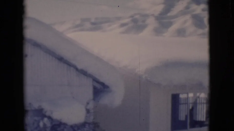 1966 8mm frame from Clarkdale, Arizona, showing a snow-covered building in front of distant winter hills.